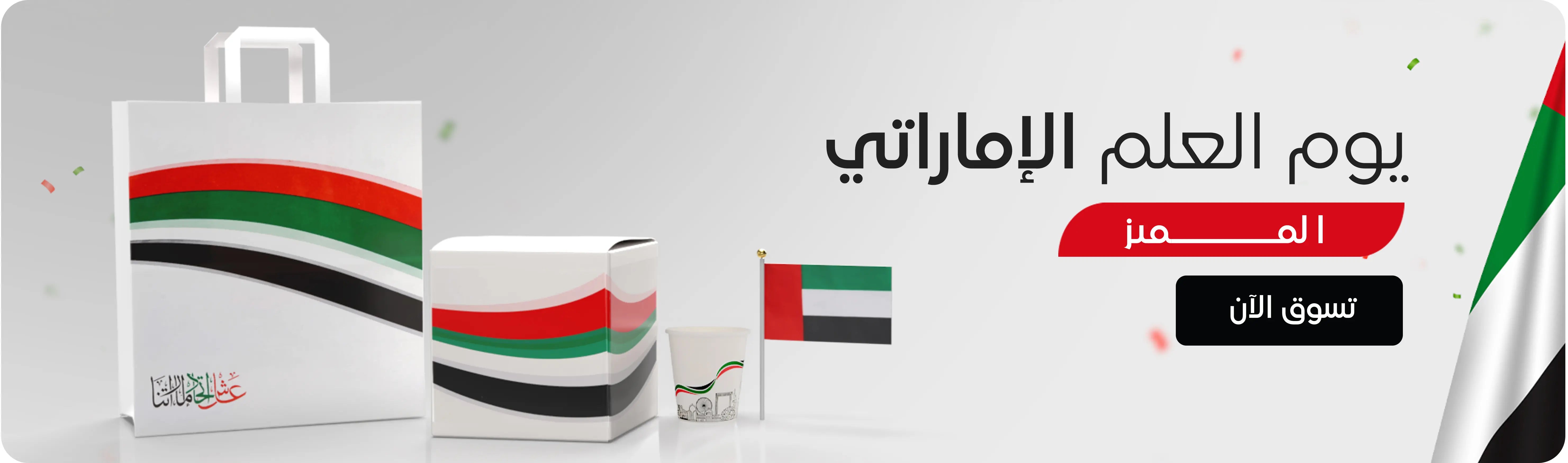 UAE Flag Day exclusive offer – white and grey banner featuring UAE flag-themed products (bag, box, cup, and small flag) with a “Shop Now” button. عرض خاص ليوم العلم الإماراتي – لافتة باللونين الأبيض والرمادي تحتوي على منتجات مزينة بألوان علم الإمارات (حقيبة، صندوق، كوب، وعلم صغير) مع زر 