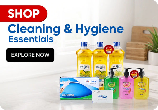 Shop Cleaning & Hygiene Essentials banner featuring Soft & Cool dish washing liquid triple pack with special offer, Soft & Cool hand wash in green, pink, and yellow variants with special offer, Hotpack clear powder-free vinyl gloves box, and Soft & Cool soap bar displayed on a bright kitchen countertop background with Explore Now call to action. | بانر تسوق مستلزمات التنظيف والعناية الصحية يعرض سائل غسيل الأطباق سوفت آند كول ثلاث قطع بعرض خاص، غسول اليدين سوفت آند كول بألوان أخضر وزهري وأصفر بعرض خاص، علبة قفازات فينيل شفافة خالية من البودرة من هوت باك، وصابون سوفت آند كول معروضة على خلفية طاولة مطبخ مضيئة مع زر إستكشف الآن.