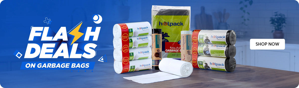 Flash Deals on Garbage Bags banner featuring Hotpack white garbage bag rolls with special offer stickers, Hotpack green garbage bags bulk pack, Hotpack black garbage bag rolls with special offer stickers, and a single white garbage bag roll displayed on a dark kitchen countertop against a blue background with Shop Now call to action. | بانر العروض الخاطفة على أكياس القمامة يعرض رولات أكياس قمامة بيضاء من هوت باك مع ملصقات عرض خاص، عبوة كبيرة من أكياس القمامة الخضراء من هوت باك، رولات أكياس قمامة سوداء من هوت باك مع ملصقات عرض خاص، ورول واحد من أكياس القمامة البيضاء معروضة على طاولة مطبخ داكنة بخلفية زرقاء مع زر تسوق الآن.