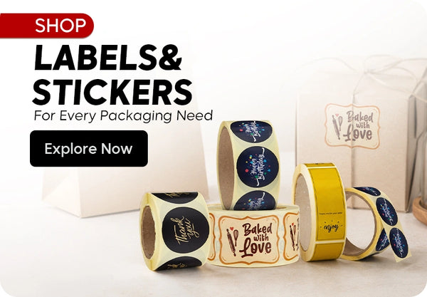 Shop Labels & Stickers For Every Packaging Need banner featuring rolls of decorative stickers including black Thank You round sticker roll, Baked with Love label roll, Happy Birthday black round sticker roll, gold enjoy sticker roll, and Baked with Love gift box displayed on a white background with Explore Now call to action. | بانر تسوق الملصقات والستيكرات لكل احتياجات التغليف يعرض رولات ملصقات زخرفية تشمل رول ملصقات شكراً لك الدائرية السوداء، رول ملصقات Baked with Love، رول ملصقات عيد ميلاد سعيد الدائرية السوداء، رول ملصقات ذهبية enjoy، وعلبة هدية Baked with Love معروضة على خلفية بيضاء مع زر تصفح الآن.